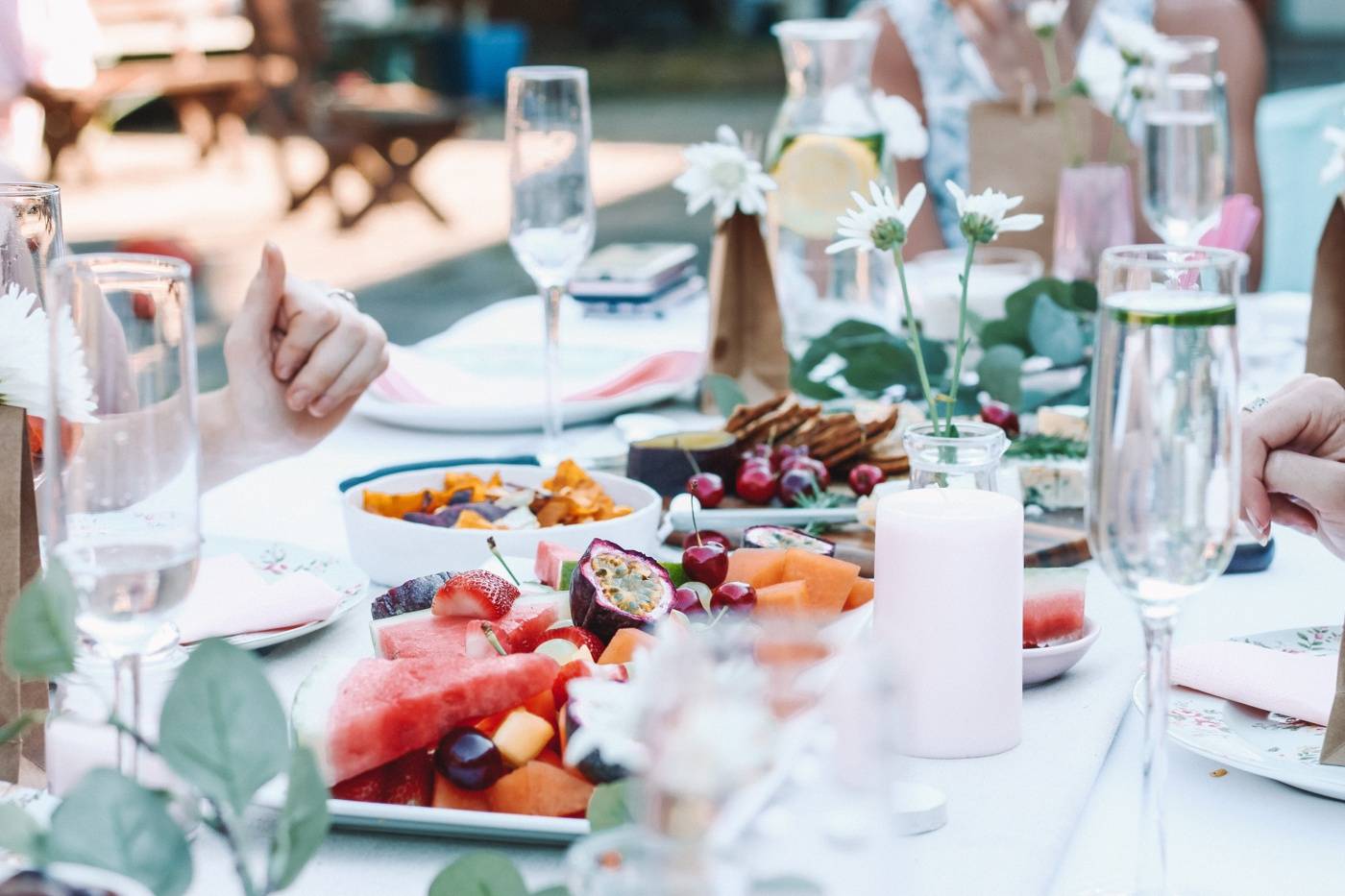 A party table with a platter of fruit, glasses of champagne, and white floral arrangements on top